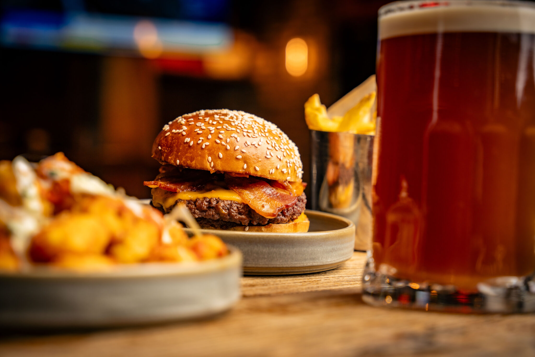 table with burger and fries on it with a beer beside it